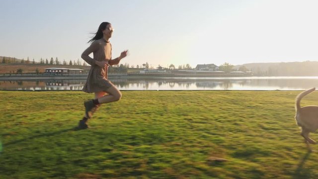 Adorable young woman playing running with her cute dog on nature near the lake.