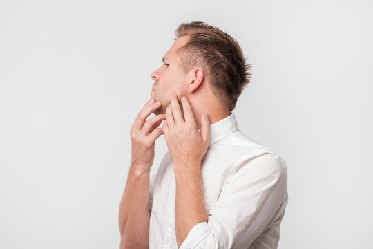 Worried European Guy In White Shirt Touching His Cheek And Look Confused