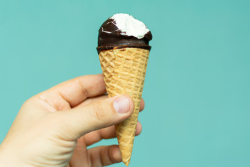 bitten vanilla ice cream in a cone and in chocolate icing on a blue background in hand