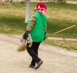 A cleaning lady is sweeping the road with a broom