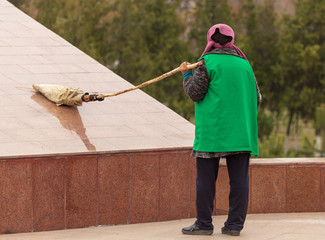 A cleaning lady is sweeping the road with a broom