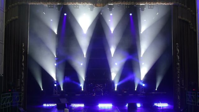 Blue light flashing and white rays on an empty stage in the dark. White and blue professional spotlights on stage at a music concert. Stage lighting. Light show.