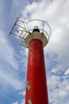 faro rojo y blanco de entrada en el puerto visto desde abajo con fondo de cielo azul con nubes