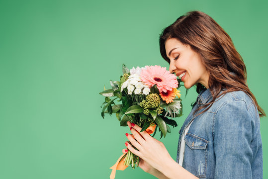 smiling woman holding and sniffing flower bouquet isolated on green
