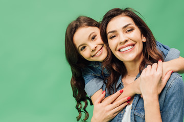 portrait of cheerful mother and daughter embracing and looking at camera isolated on green