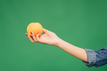 cropped view of woman holding orange in hand isolated on green