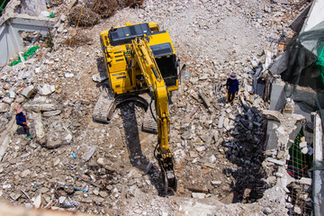 The backhoe machinery working on site demolition of an old building workers spray water to get rid of dust.