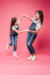 happy daughter in rollerblades holding hands with mother on pink background