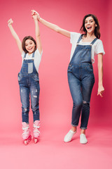 happy daughter in rollerblades cheering and holding hands with mother on pink background