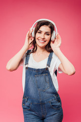 smiling woman listening music in headphones isolated on pink