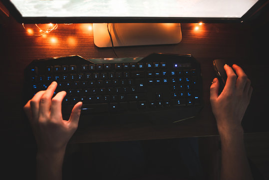 Man Uses A Computer At Night, Hands On The Keyboard And A Mouse Over The Top. Mouse And Keyboard Game Player. Man Plays Video Games On A Computer, The Look Of The Hands From Above. Flat Lay