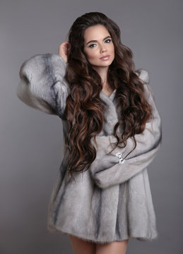 Elegant woman in mink fur coat isolated on gray studio background. Brunette Girl in Luxury Winter outerwear.