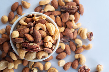 roasted mixed nuts in white ceramic bowl on barble table background.