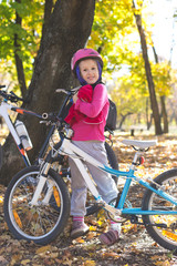 Cute little girl with a bicycle in the autumn forest