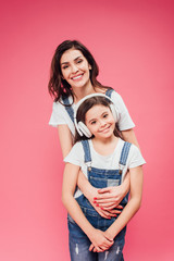 mother hugging daughter in headphones isolated on pink