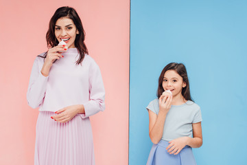 beautiful woman and child eating cupcakes and looking at camera on blue and pink background