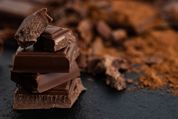 Broken chocolate pieces and cocoa powder on a dark background