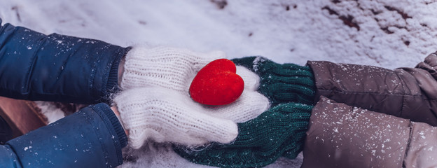 Hands in gloves holding heart closeup on winter snow background. Toned. Valentine's Day and love concept, banner