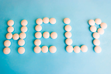 Beautiful inscription help made from white round smooth medical pills, vitamins, antibiotics and copy space on a bright blue background. Flat lay