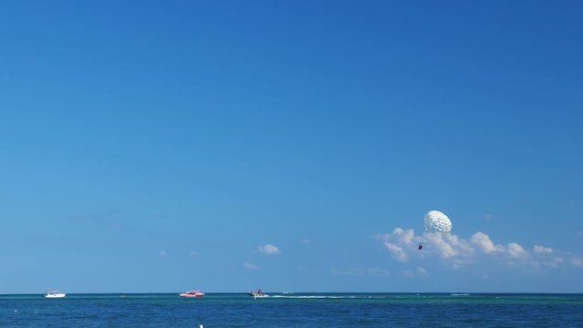 Parasailing from boat under caribbean sea, tourists having fun on vacations
