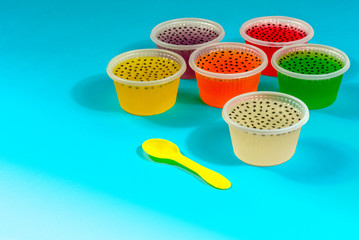 Colorful of homemade fruit gelatin mixed grain seeds in plastic cups with spoon isolated on cyan background with clipping path.