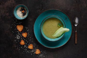 Vegetarian cauliflower and broccoli homemade cream-soup with seeds, heart shape crackers and fresh seasoning.  Close up, top view, flat lay  on the dark wooden background