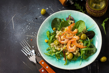 Diet menu, Vegan food. Healthy salad with quinoa, arugula, Shrimps and olives on a dark stone table.