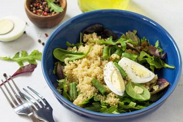 Diet menu, Vegan food. Healthy salad with quinoa, arugula, green Beans and Eggs on a white stone table.