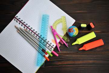 stationery with a globe and markers spread out on a notebook lying on a dark wooden table, top view - Powered by Adobe
