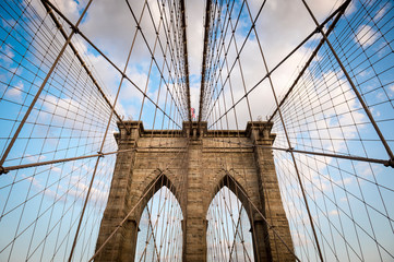 Classic view of the steel cable pattern and rough brick details of a stone tower of the Brooklyn Bridge under soft picturesque clouds