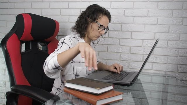 A woman at the computer shows the middle finger. A busy woman at the workplace behind a laptop shows an indecent gesture.