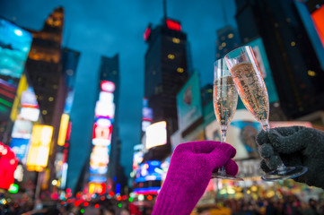 Gloved hands holding up Champagne glasses in a Mew Year’s Eve toast against the bright lights of...