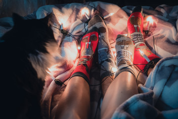 Legs wearing Christmas socks on fluffy cover with light garland
