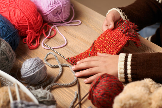 Child boy is learning to knit. Colorful wool yarns are on the wooden table. Hand closeup.