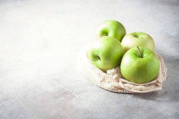 Organic green apples in reusable cotton net bag on wooden table. Eco-package, zero waste concept.
