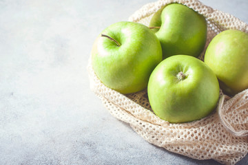 Organic green apples in reusable cotton net bag on wooden table. Eco-package, zero waste concept.