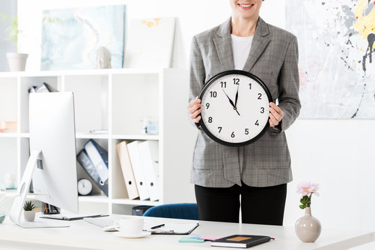 cropped image of attractive businesswoman holding wall clock in office