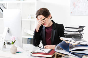 sad exhausted businesswoman touching forehead at table in office