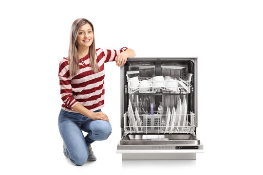 Beautiful young woman kneeling next to an open dishwasher