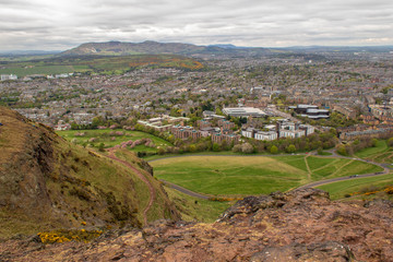 Fototapeta na wymiar Urban landscape of Edinburgh in Scotland, as seen from Arthur's Seat peak. Cityscape on a Spring day with distant green hills and cherry blossom trees.