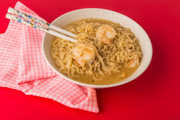 Bowl of Chineese Noodles and Shrimp with Chopsticks against red background