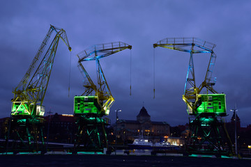 Colorfully illuminated antique cranes on the quay of Szczecin Łasztownia. - obrazy, fototapety, plakaty