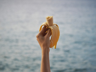 A bitten yellow banana in a woman's hand. ocean background