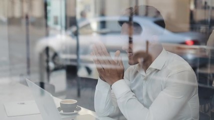 Happy young business sitting at a table in a cafe working on a laptop. Winner looking at laptop showing yes gesture, celebrating success, good news on web, enjoying triumph, did it