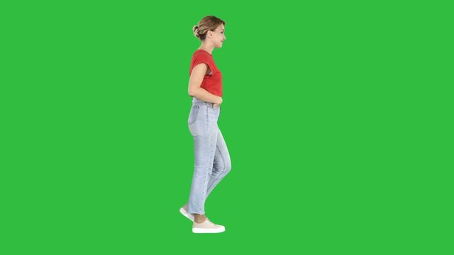 Fit girl holding her hands in the pockets of blue jeans walking on a Green Screen, Chroma Key.