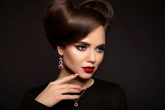 Elegant lady with jewelry set. Beautiful woman with makeup and retro hairstyle, presenting precious earrings and necklace isolated on studio dark background. Beauty and accessories.