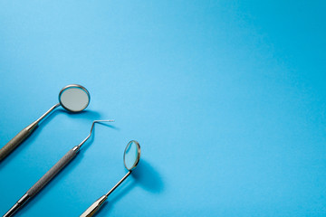 Dentist tools: two mirrors, dental probe and tweezers lying on blue background.