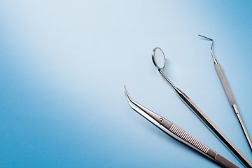 Dentist tools: mirror, dental explorer and tweezers in right on blue gradient background.