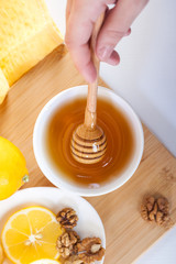 honey in a white ceramic bowl with honey dipper and lemon on a wooden kitchen boar