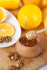 honey in a wooden bowl with honey dipper and lemon on a wooden kitchen board